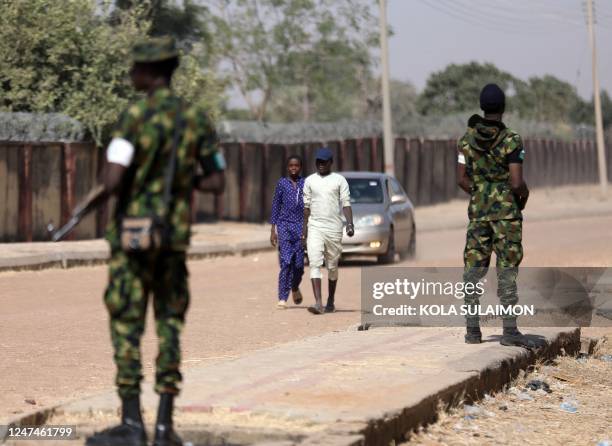 People walk past Nigerian army officers near a polling station at Kwankwaso ward, Malamai in Kano on February 25 during Nigeria's presidential and...