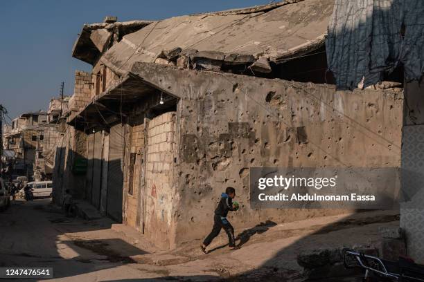 Syrian child plays with a ball next to a perforated wall because of the war in the city of Harim, on February 24, 2023 north of Idlib, Syria....