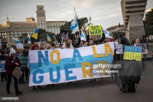 People, holding banners and various flags, gather to stage a protest against war on the first anniversary of the Russia-Ukraine war, at Placa de Sant...