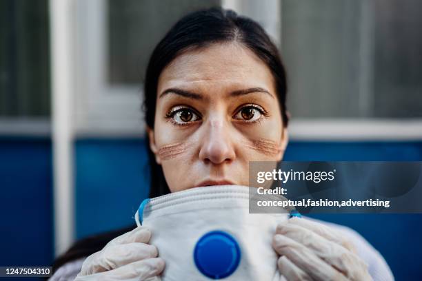 exhausted doctor / nurse taking of coronavirus protective gear n95 mask uniform.coronavirus covid-19 outbrek.mental state of medical professional.face scars.mask shortage.overworked health workers - n95 respirator mask stock-fotos und bilder