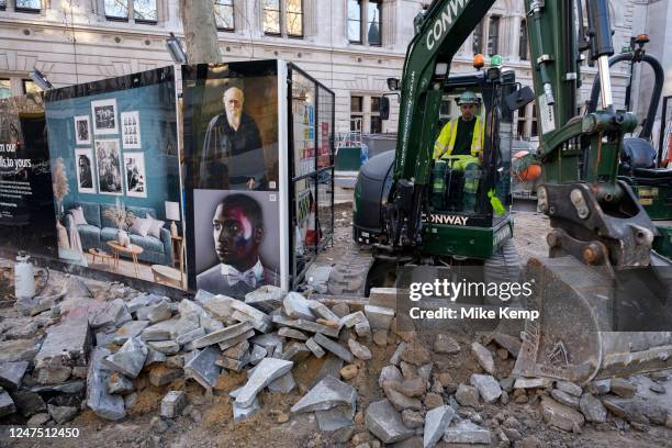 Worker operating a small digger interacts with classic portraits of well known or famous people from contemporary culture including Charles Darwin...