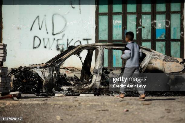 Palestinian boy walks near a burned car after settlers riot and set houses and cars on fire in the village of Hawara on February 27, 2023 in Hawara,...