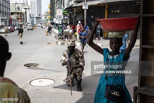 Young girl carries a bucket past a soldier from the Nigerian Armed Forces, as he takes position in the streets of Lagos Island, Lagos, on February 27...