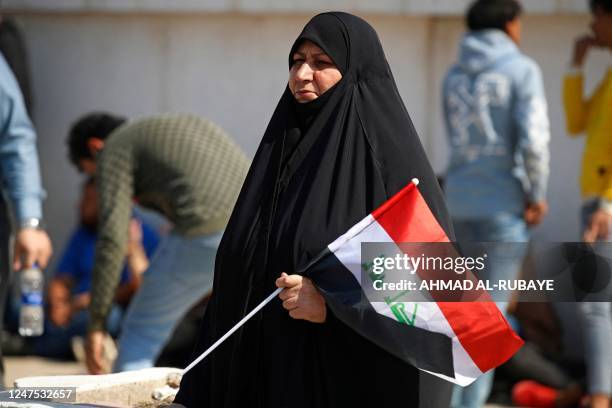 Woman lifts a national flag during a protest near Baghdad's Green Zone on February 27, 2023 as the Iraqi Parliament convenes to amend the electoral...