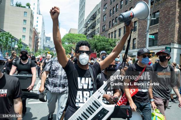 Musician Jon Batiste wearing a mask holds up his hands while his band jams for the crowd of people that have followed him onto to 6th Avenue from...