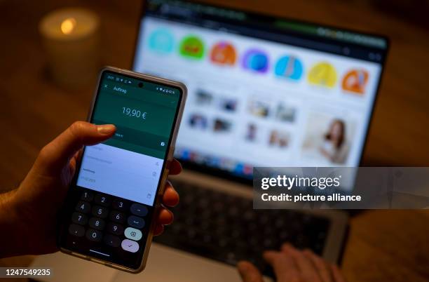 February 2023, Berlin: A man transfers money in a banking app on a smartphone while the page of an online retailer is displayed in the background on...