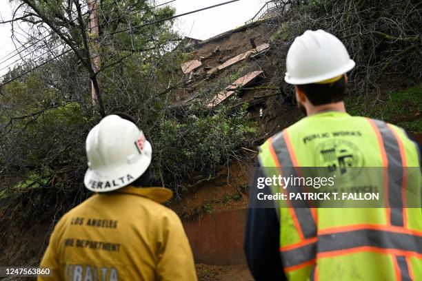 Firefighter and public works crew member look at the damaged hillside from mud flows and a landslide below a home above Mulholland Drive following...