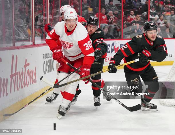 Shane Pinto and Alex DeBrincat of the Ottawa Senators battle for puck possession against Robert Hagg of the Detroit Red Wings at Canadian Tire Centre...