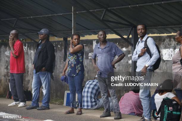 People wait for a bus in the street in Libreville on February 28, 2023.