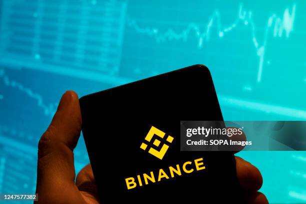 In this photo illustration, the cryptocurrency exchange trading platform Binance logo is seen displayed on a smartphone with an economic stock...