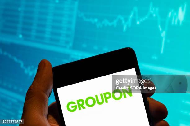 In this photo illustration, the American worldwide e-commerce marketplace Groupon logo is seen displayed on a smartphone with an economic stock...