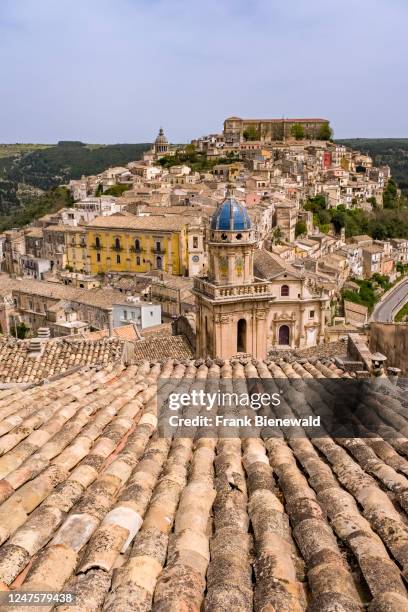 Aerial view of the Late Baroque town of Ragusa Ibla, perched on a hill, seen over the tiles of a roof.