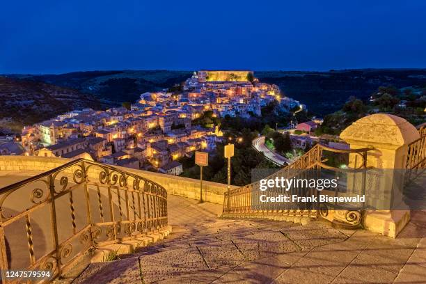 Aerial view of the Late Baroque town of Ragusa Ibla, perched on a hill, seen from the steps of a staircase, illuminated at night.