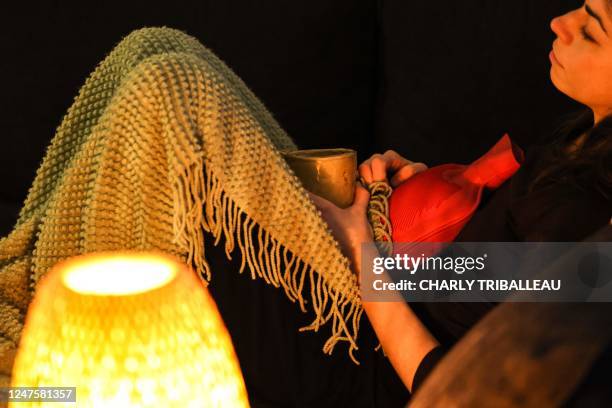 This illustration photograph taken on March 1, 2023 shows a woman with painful periods lying on a sofa while holding a hot water bottle in Toulouse,...