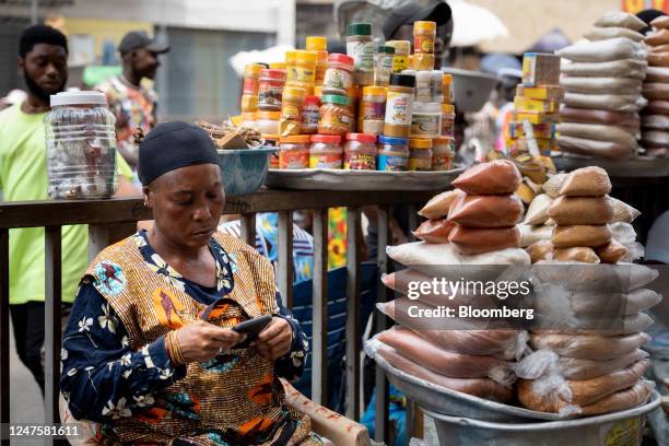 Street vendor checks her phone whilst waiting for customers in Accra, Ghana, on Tuesday, Feb. 28, 2023. Ghanas cedi, the worlds second-worst...