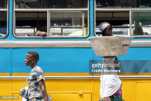 Street vendors pass a stationary bus in the Makola district of Accra, Ghana, on Tuesday, Feb. 28, 2023. Ghanas cedi, the worlds second-worst...