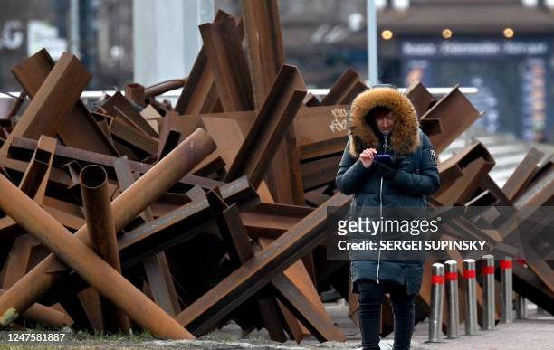 Woman looks at her phone as she walks past anty tank constructions in the center of Kyiv on March 1, 2023.