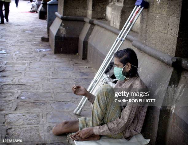 An Indian amputee wearing a mask, sits on the sidewalk with his hand out waiting for donations from passing pedestrians in the streets of Bombay, 10...