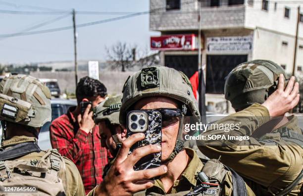 An Israeli soldier takes photos with his phone, during a protest against the attacks of the Jewish settlers and the closure of the commercial stores...