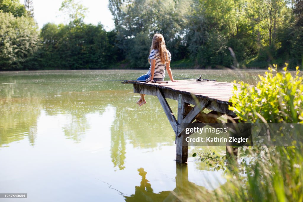 Woman sitting on jetty with two fishing rods