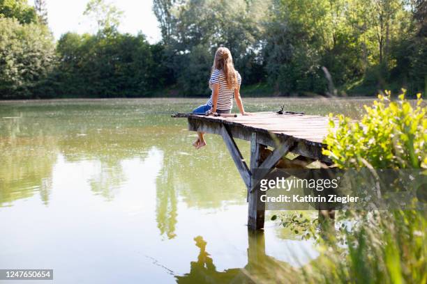 woman sitting on jetty with two fishing rods - freizeit stock-fotos und bilder