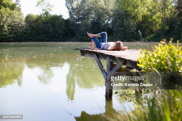 woman reclining on jetty with two fishing rods - low key stock-fotos und bilder