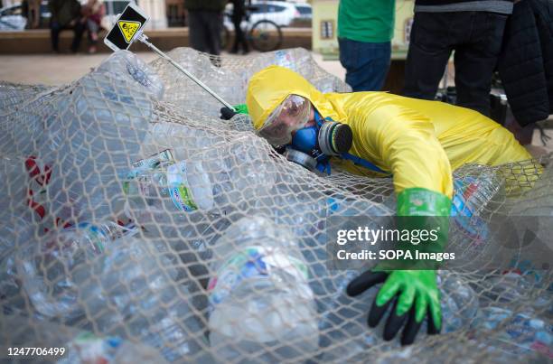 Man dressed in overalls is seen embracing plastic bottles during a protest against climate change. Dozens of people and environmental organizations...