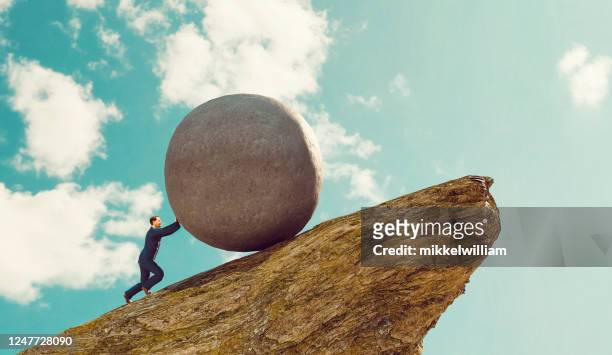 concept de travail acharné pour l’homme d’affaires poussant le rocher vers le haut d’une colline - irréductibilité photos et images de collection
