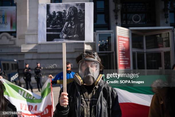 Man wearing a gas mask holds a placard with a drawing of a girl wearing gas masks in Iran during the demonstration. Iranian citizens residing in...