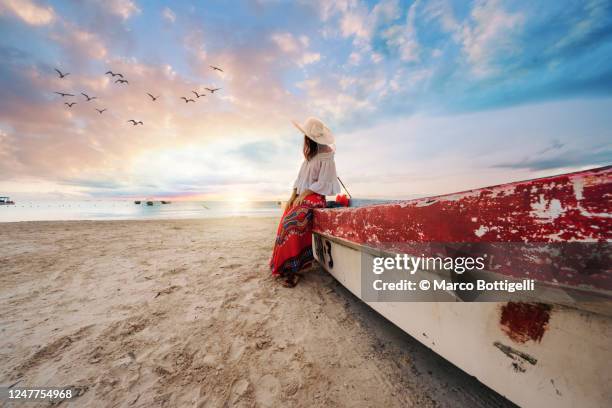 woman leaning against a boat on a beach at sunset, tulum, mexico - mexico sunset stock pictures, royalty-free photos & images