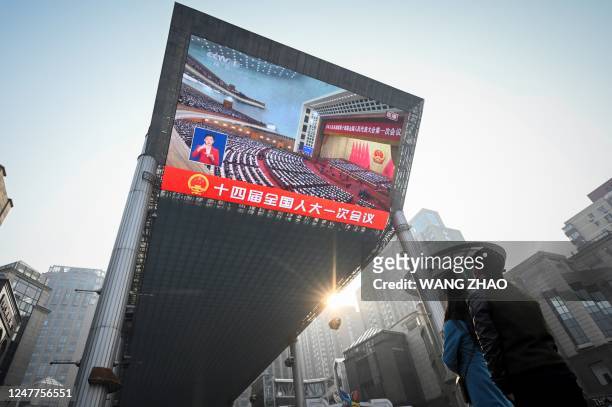 People watch live coverage of the opening session of the National Peoples Congress on an outdoor screen in Beijing on March 5, 2023.