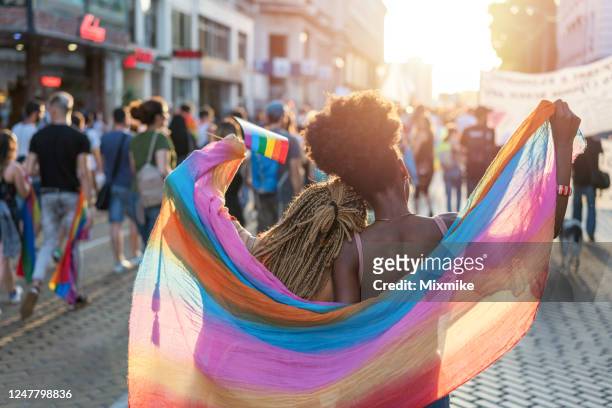 coppia femminile che cammina con la parata dell'orgoglio - gay pride flag foto e immagini stock