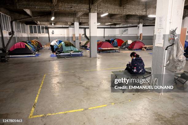 Woman looks at her smartphone in a parking lot transformed by the humanitarian association Utopia 56 into a temporary night shelter with tents near...