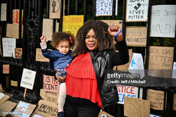 Woman holding a child, raise their fists in the air as Black Lives Matter protesters hang their banners on the fence of Holyrood Palace, despite a...