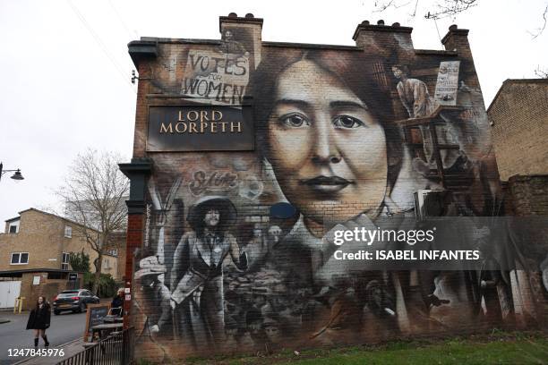 Schoolgirl passes a large mural depicting suffragette Sylvia Pankhurst, created in 2018 by Australian artist Jerome Davenport on the wall of a pub in...