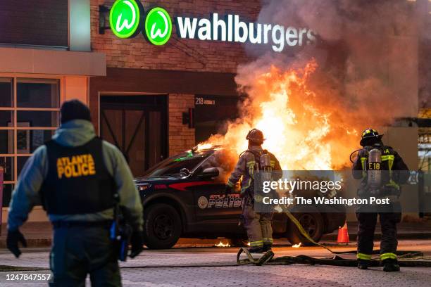 Firefighters are seen in front of a burning police vehicle during a protest following the shooting death of Manuel Teran during a police raid on...