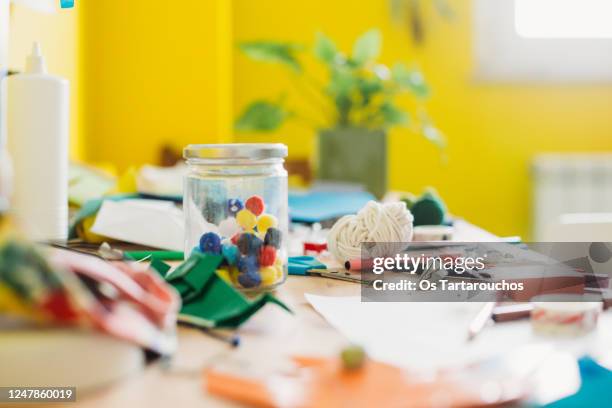 jar with color pompoms on a messy desk full of craft supplies - craft table stock pictures, royalty-free photos & images