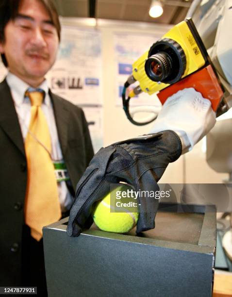 Man watches a soft robot hand with a CCD camera, developed by Japanese robot venture Squse, catches a tennis ball during a demonstration at the...