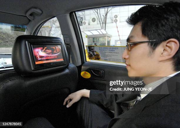 Passenger looks at a liquid crystal display screen, situated in the back of the headrest on the front passenger seat in a taxi, showing...