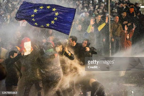 Protesters brandishing a European Union flag brace as they are sprayed by a water cannon during clashes with riot police near the Georgian parliament...