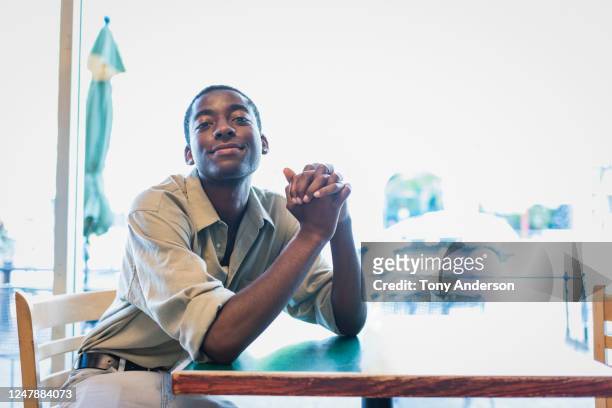 young man sitting at table in cafe - sitting at table looking at camera stock pictures, royalty-free photos & images