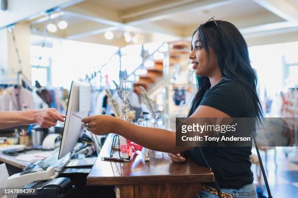 young woman paying cashier in clothing store - kaufsucht stock-fotos und bilder