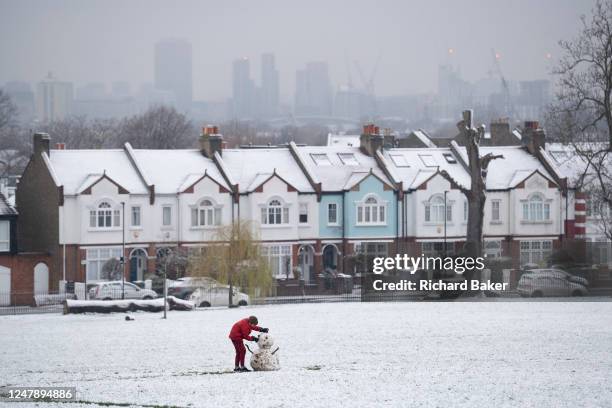 As March snow falls on south London, a boy builds a small snowman in front of period homes, in Ruskin Park, a public green space in Lambeth, on 8th...