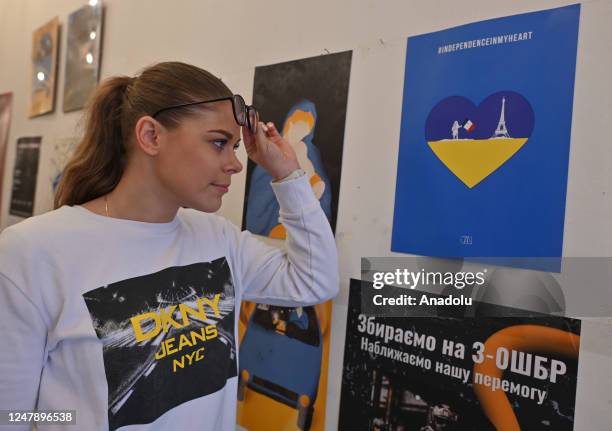 Sylwia Pieczara, a journalist at TVP Krakow, takes a closer look at the Ukrainian poster exhibition at NIC Cafe, on March 7 in Krakow, Poland. Even...