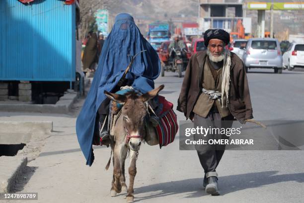 Man walks beside a burqa-clad woman riding a donkey along a street in Fayzabad on March 8, 2023.