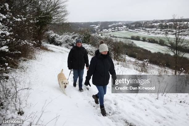 Couple walk their dog in the snow at Dartland Banks nature reserve near Hampstead on March 8, 2023 near Sevenoaks, United Kingdom. A yellow weather...