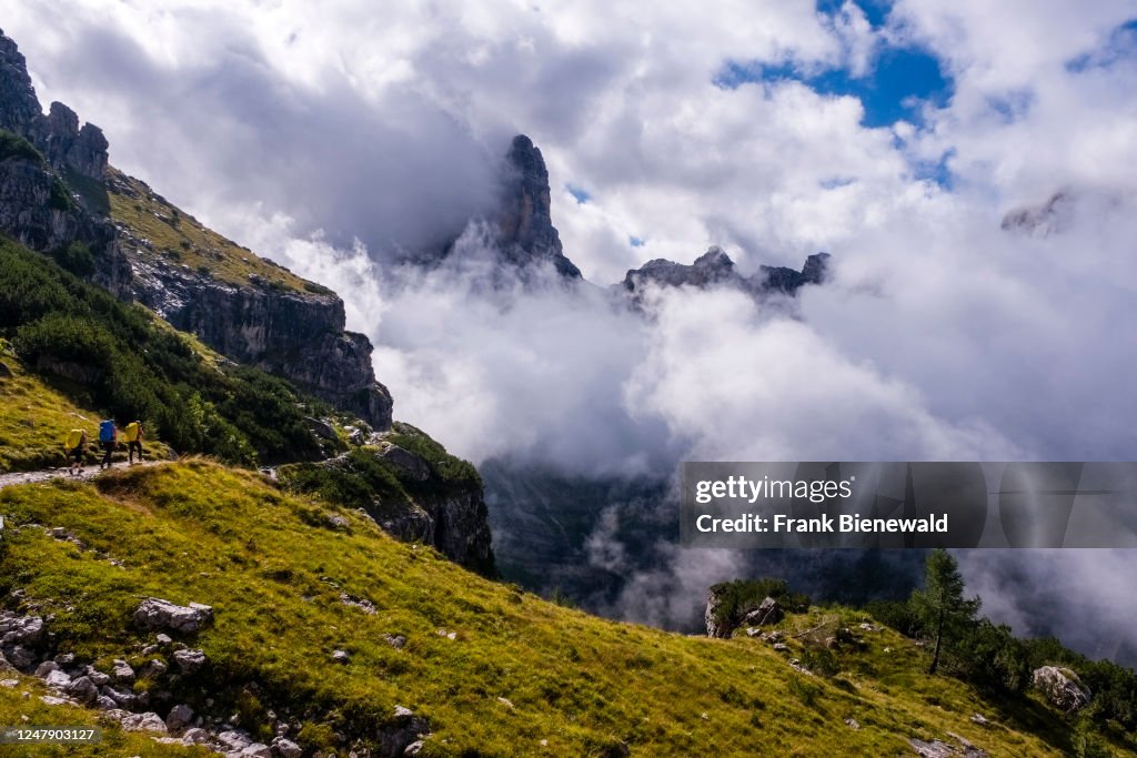 Three hikers walking on a path in Brenta Dolomites, summits