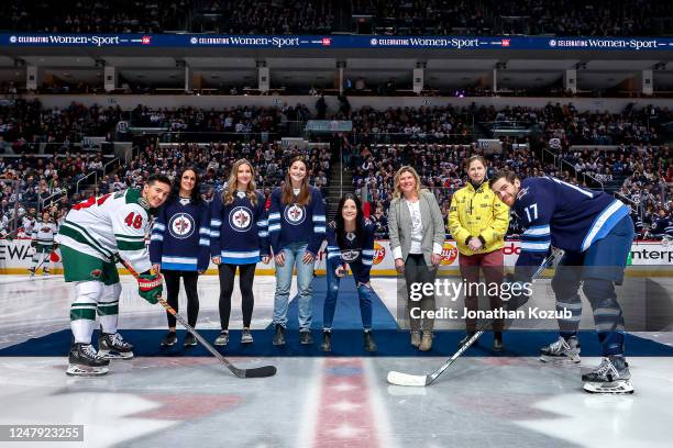 Jared Spurgeon of the Minnesota Wild and Adam Lowry of the Winnipeg Jets take part in the ceremonial face-off on Celebrating Women In Sport Night at...