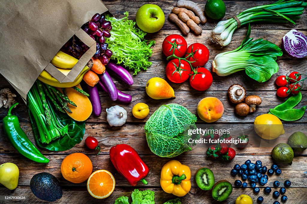 Shopping bag filled with fresh organic fruits and vegetables shot from above on wooden table