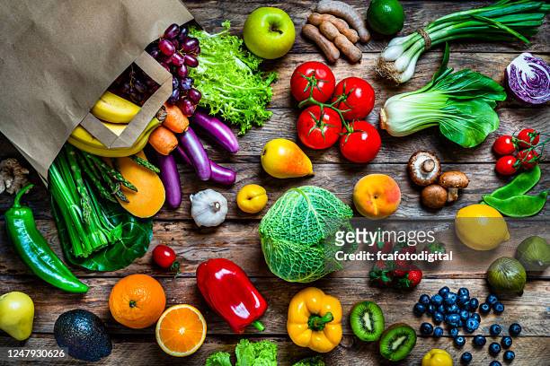 shopping bag filled with fresh organic fruits and vegetables shot from above on wooden table - vegetable stock pictures, royalty-free photos & images